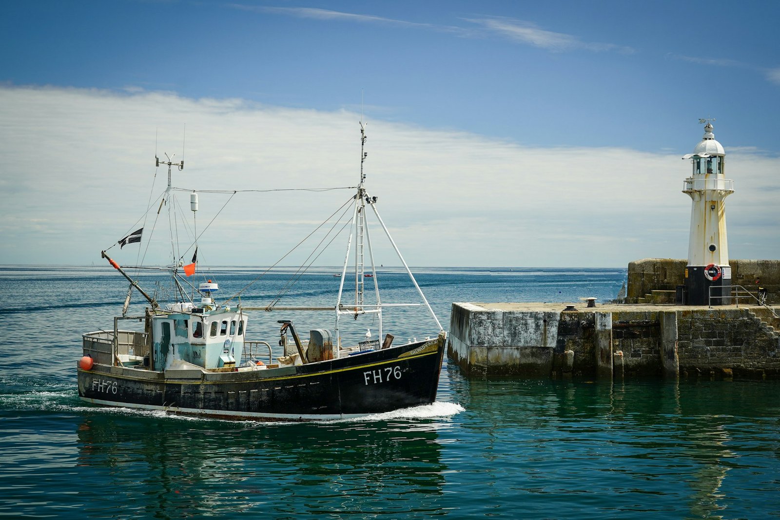 Fishing boat entering a UK harbour near a lighthouse