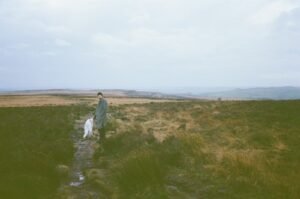 Person and dog on a muddy path across grassland