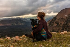 Woman sitting beside a black dog on a hillside