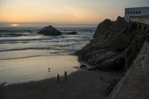 People and a dog on a sandy beach below rocky cliffs